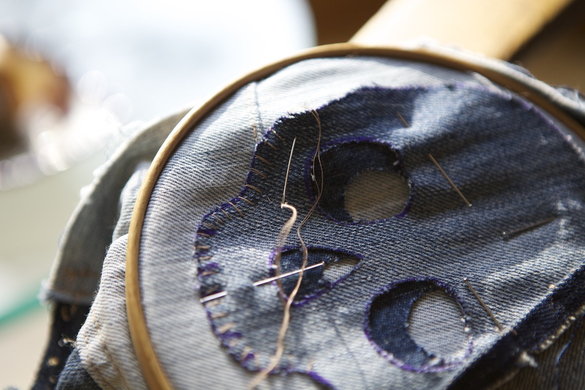 Close-up of the Modern Mending skull patch being hand stitched on jeans.
